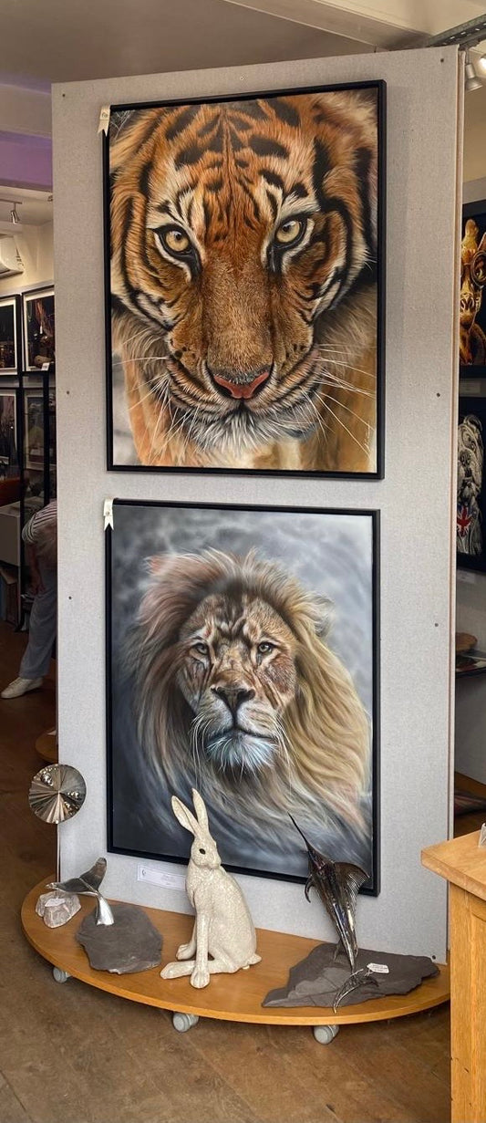 A tall display stand showcasing two large framed animal portraits by artist Andy Caddick. Photo at The Acorn Gallery in Pocklington. TOP:Silent Sovereign (Tiger) BOTTOM: Always Here For You (Lion). Other framed artwork in the background.