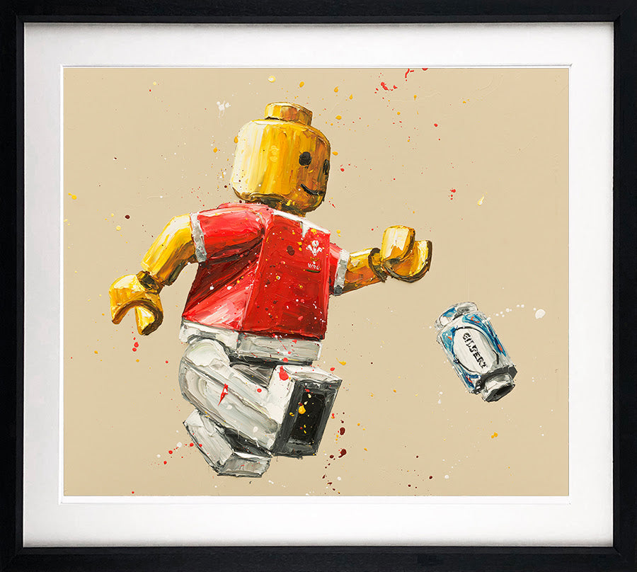 Framed Paul Oz paper print of a yellow-headed Lego rugby player in a red shirt and white shorts, with a blue boot.