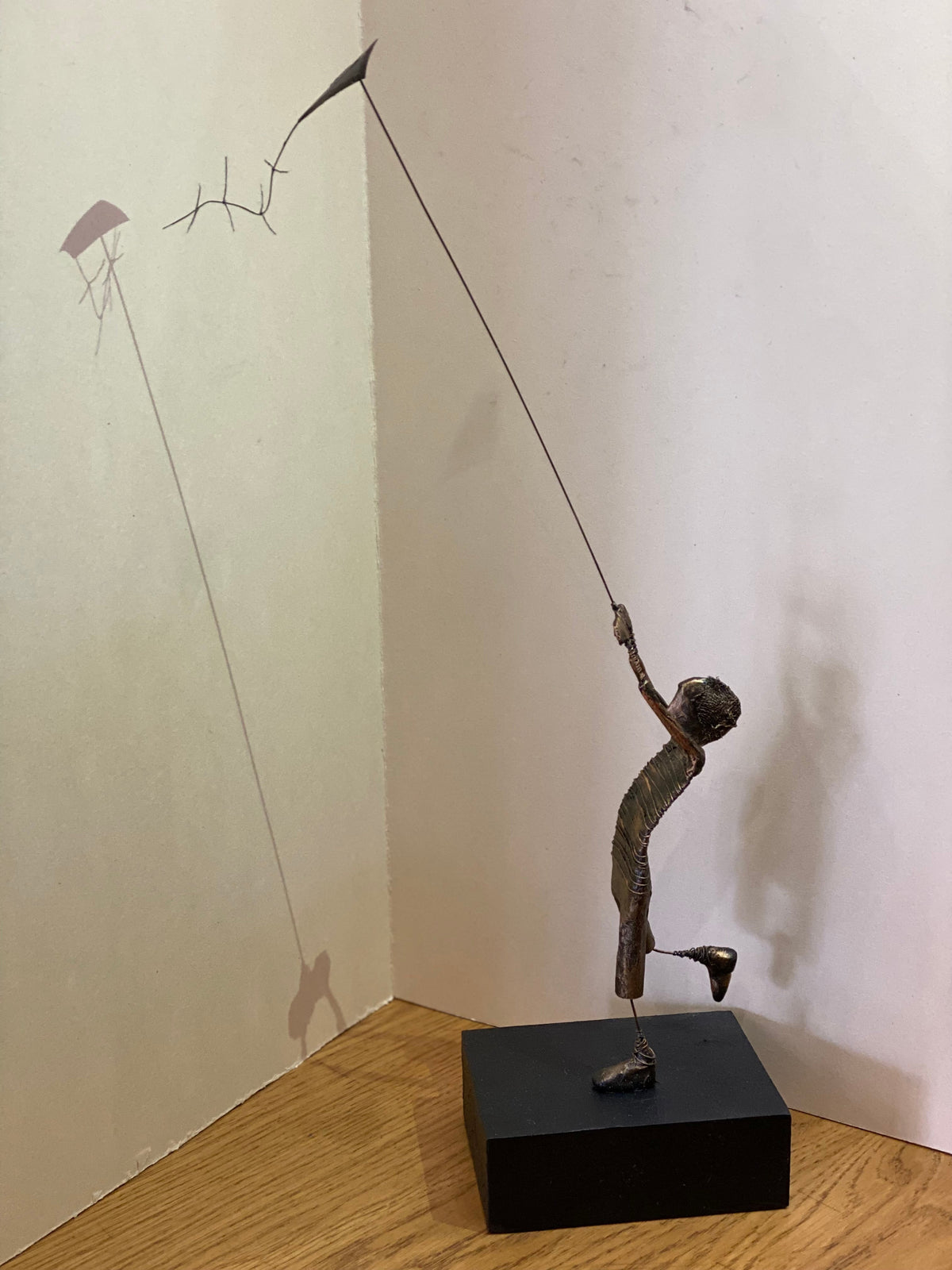 Kite-flying boy sculpture by Ed Rust , with a dark bronze-toned figure holding a long wire kite string on a black base.