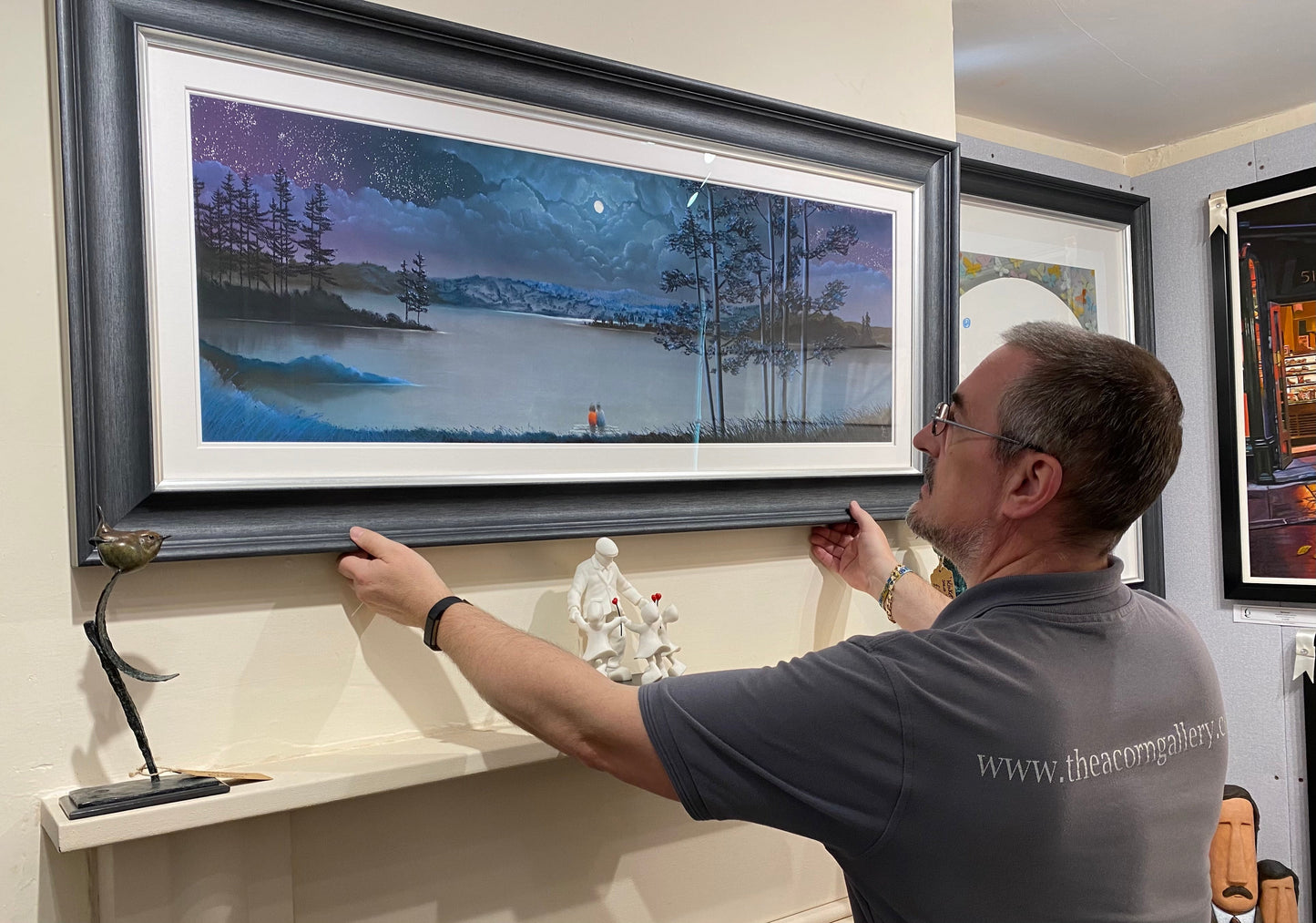 Man hanging framed original pastel artwork "Making A Wish" by Mackenzie Thorpe in gallery setting