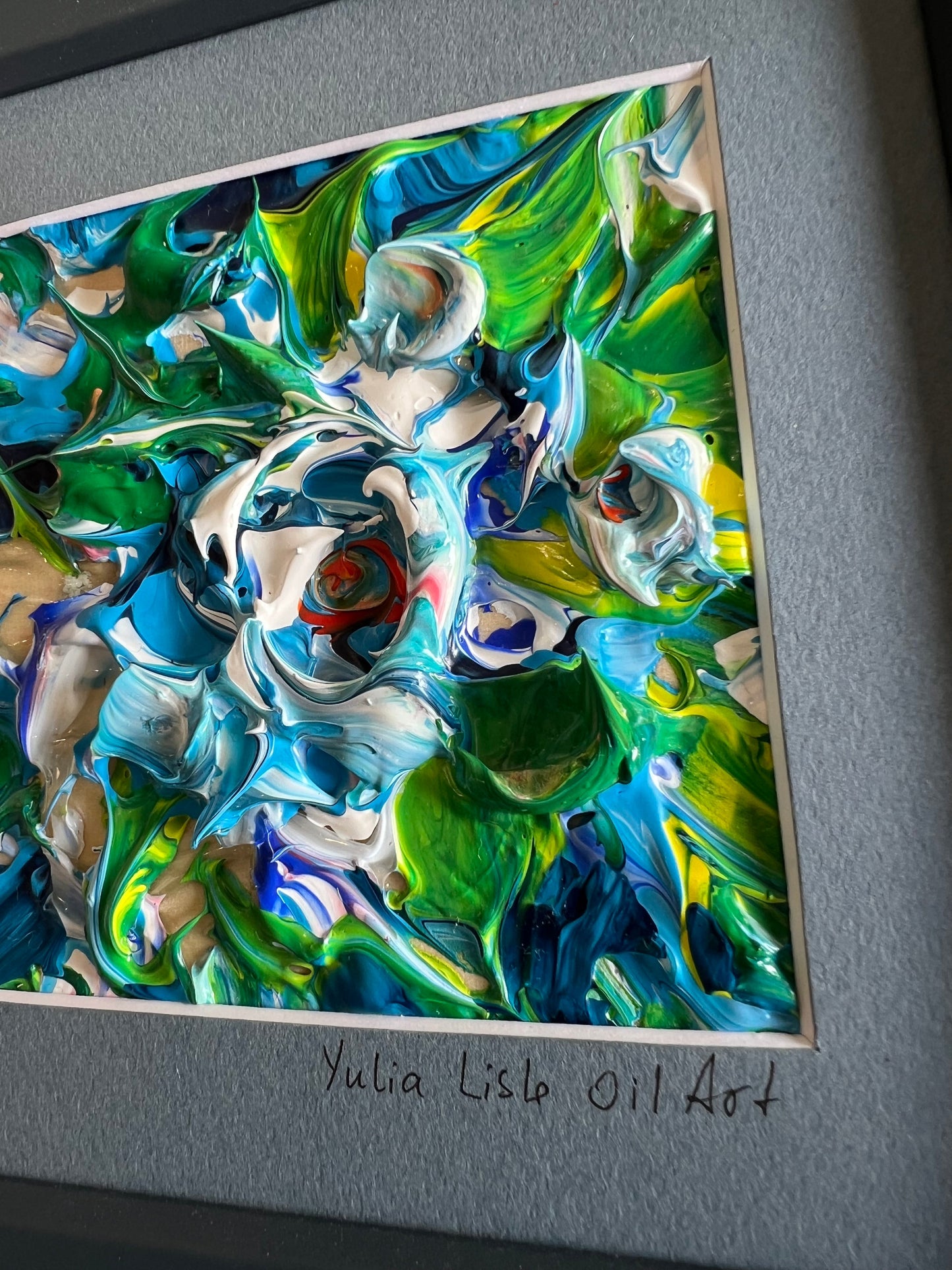 Small freestanding framed original impasto oil painting by Yulia Lisle featuring an abstract blue and white flower with vibrant green foliage, richly textured with thick palette knife strokes. Art work by Yulia Lisle and available at The Acorn Gallery in Pocklington. Shop online or call us on 01759 307652. 