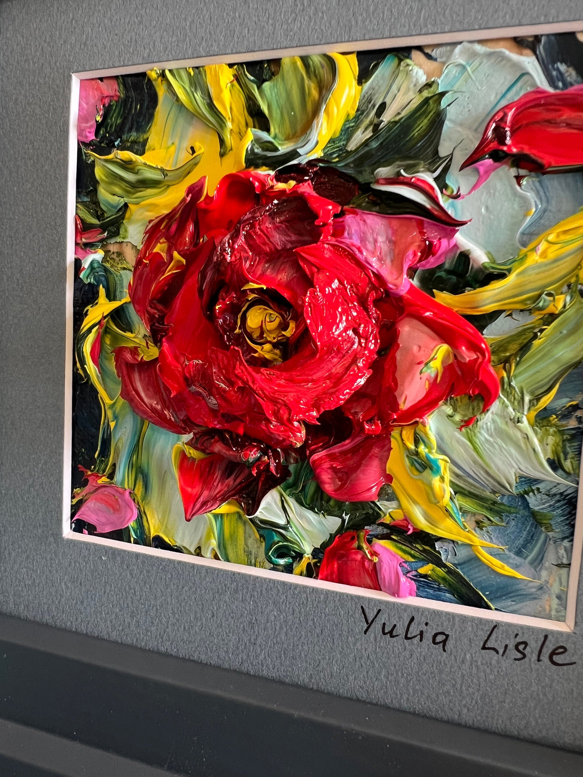 Small framed original impasto oil painting by Yulia Lisle featuring a richly textured deep red flower surrounded by vibrant green, blue and yellow foliage, created with expressive palette knife strokes. Artwork by Yulia Lisle and available at The Acorn Gallery in Pocklington where you can shop online or call us on 01759 307652.