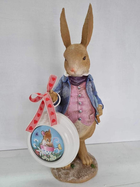 Rabbit figurine by Marie Louise Wrightson, tan rabbit in a blue jacket and pink waistcoat holding a heart-patterned ribbon and round picture frame.