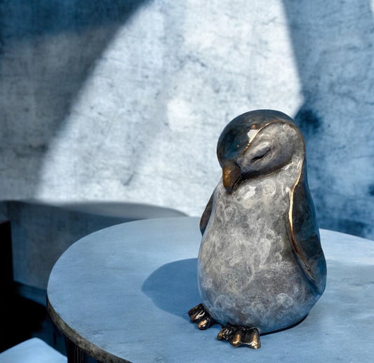 Bronze penguin sculpture with a mottled grey belly, dark patinated head and back, and bowed sleeping pose.