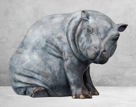 Bronze hippo sculpture in blue-gray tones, sat on her back legs, with a rounded body, and detailed face.