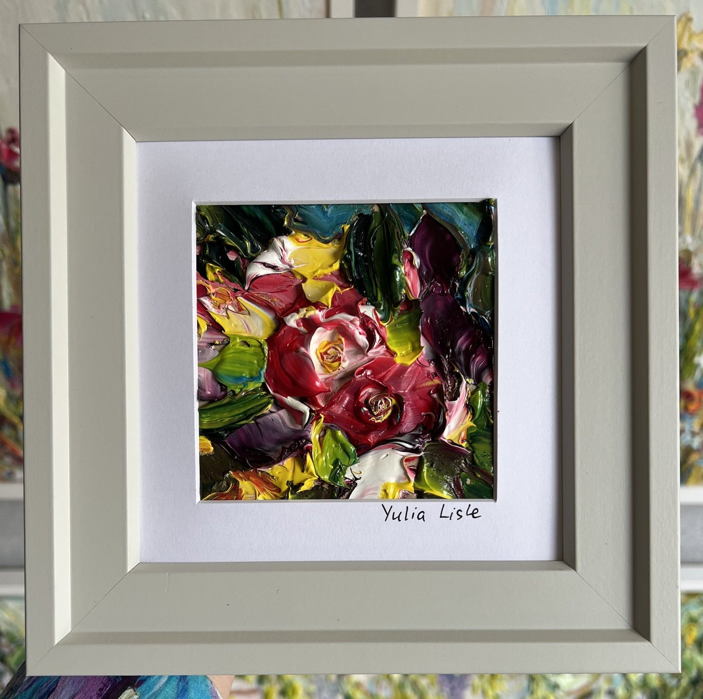 Small framed original impasto oil painting by Yulia Lisle featuring richly textured crimson flowers surrounded by vibrant green foliage, created with thick palette knife strokes and presented in a white frame. Artwork by Yulia Lisle is available at The Acorn Gallery in Pocklington. Shop online or call us on 01759 307652. 